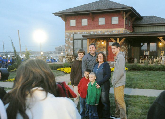 family posing in front of extreme makeover house