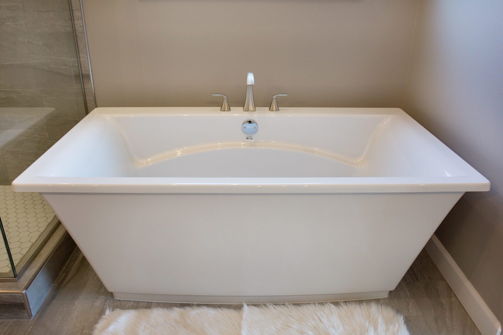 large rectangular bathtub with faucet and fur rug